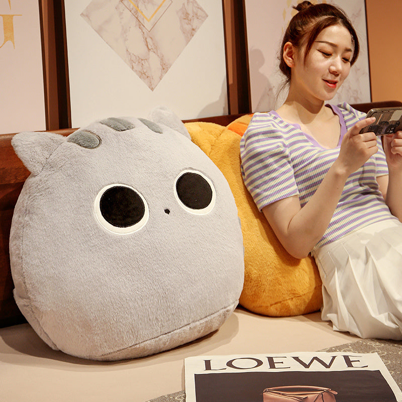 Woman sitting on a couch with a large gray cat-shaped pillow next to her, holding a phone.