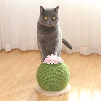 Gray cat standing on a green cat toy with a pink flower on a wooden floor.