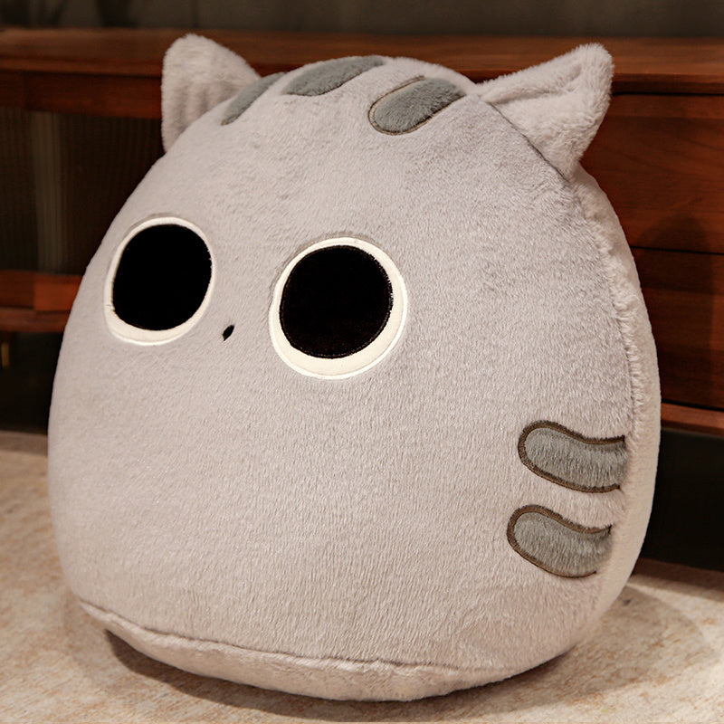 Plush cat-shaped pillow with large black eyes and paw prints on a wooden surface.