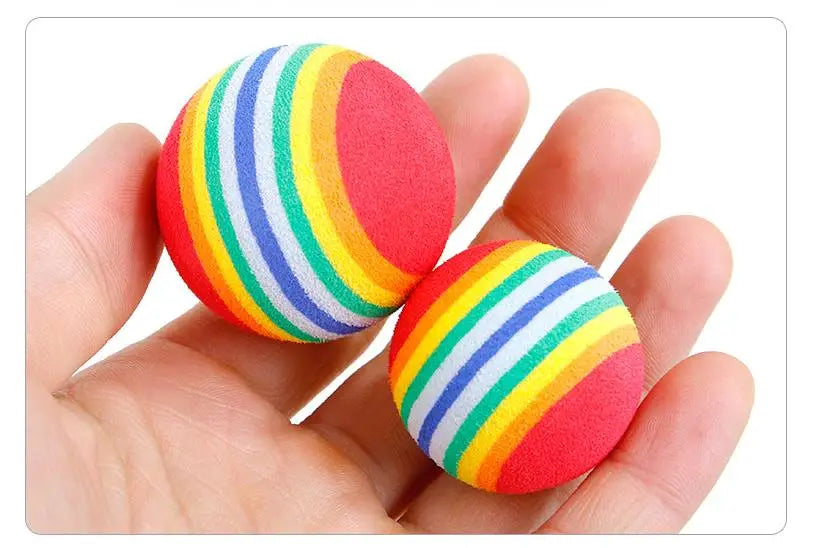 Two rainbow-striped foam balls held in a hand against a white background