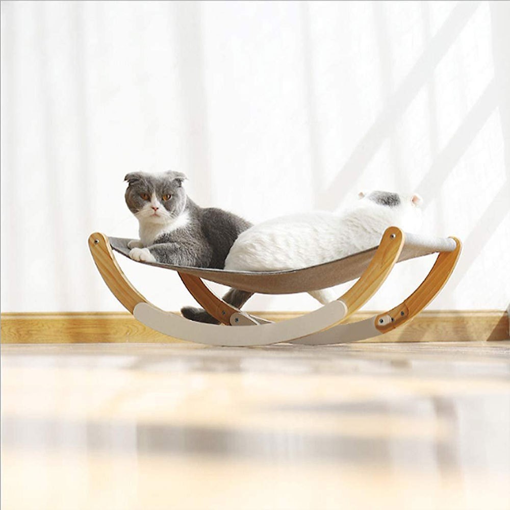 Cat lying on a wooden cat hammock with a white curtain in the background