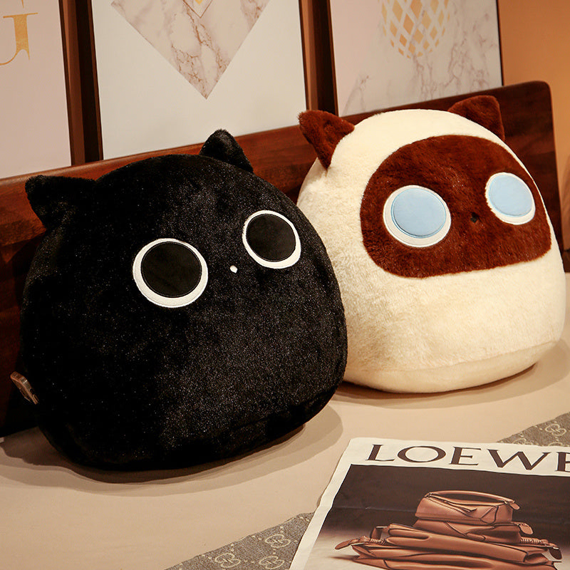 Two plush toys resembling a black cat and a white and brown creature on a surface with a magazine in the background.